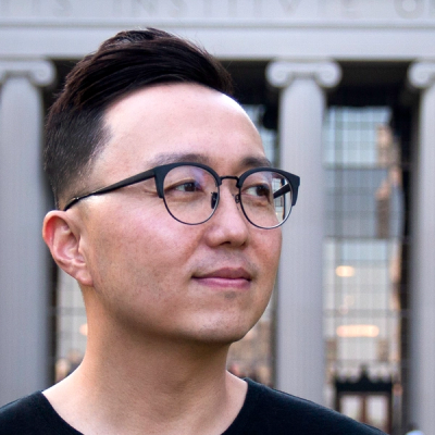 Man with dark hair wearing glasses, looking to the right. Columns from an MIT building in the background. 